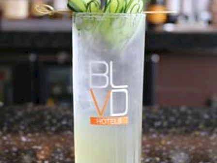 A tall cocktail glass garnished with cucumber slices, containing a light-colored beverage, with 