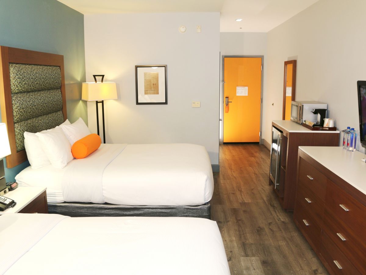 This image shows a hotel room with two beds, a TV, dresser, microwave, fridge, and a door to the hallway.