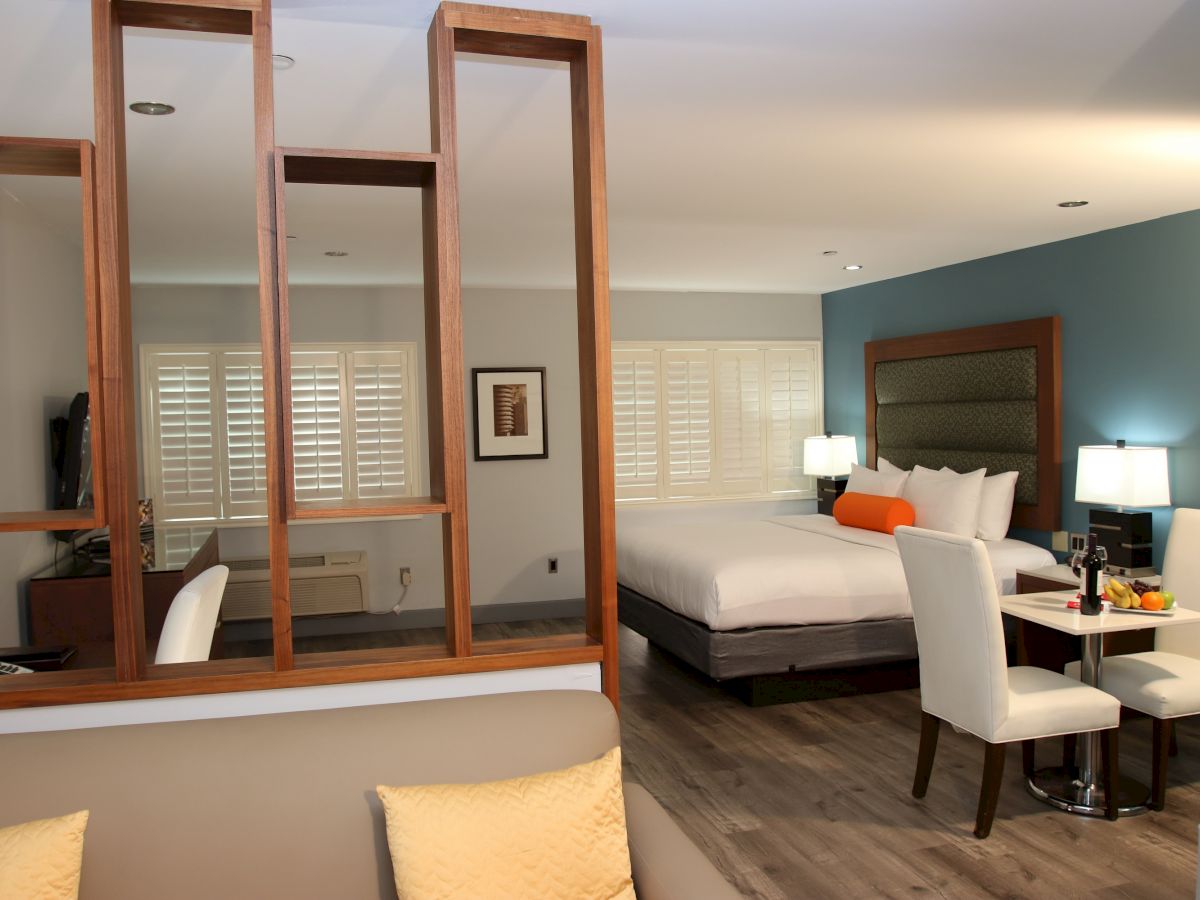 A modern hotel room featuring a partition, a bed, a desk, a small dining table with chairs, and a cozy ambiance with decorative lighting and accents.