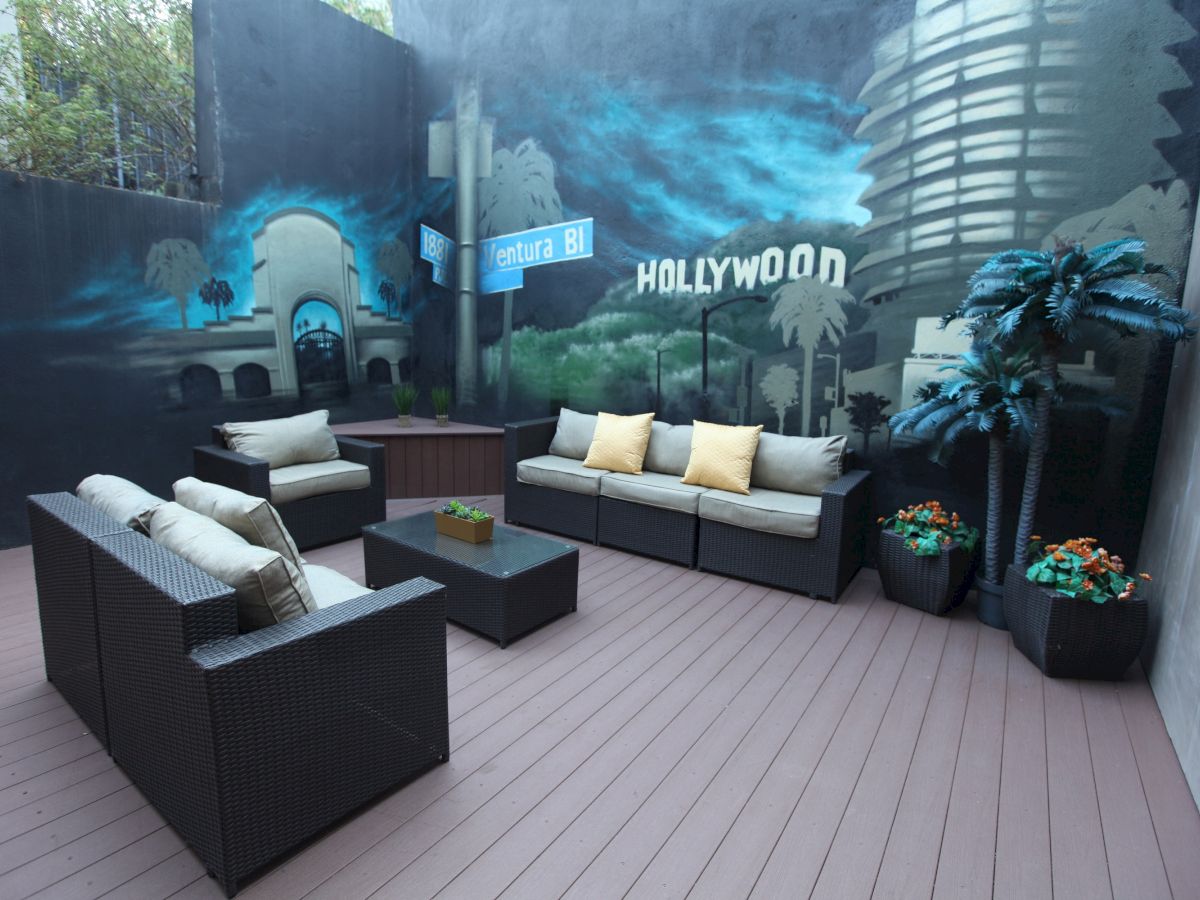 The image shows an outdoor patio with wicker furniture and cushions, a mural with 