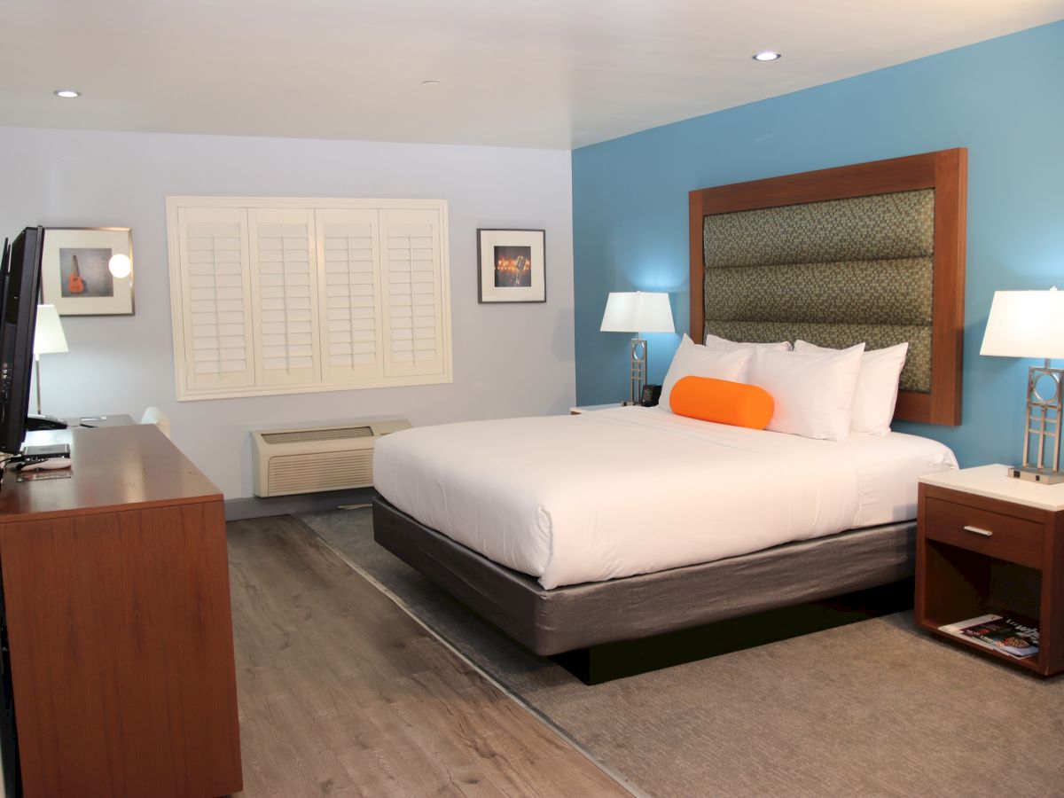 A well-furnished hotel room with a king-size bed, two side tables with lamps, a flat-screen TV, and a dresser. The accent wall is blue.