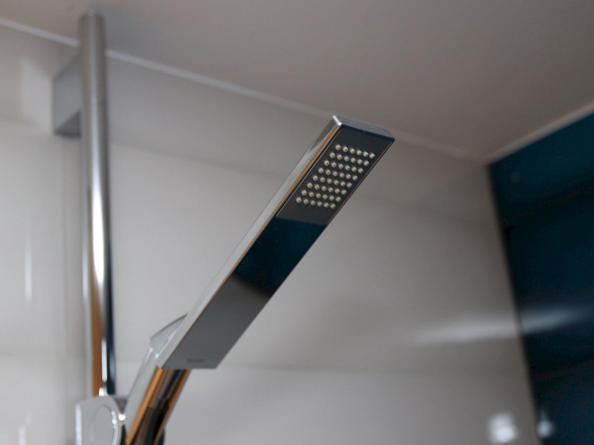 This image shows a modern, rectangular chrome shower head mounted on a shower wall in a bathroom.