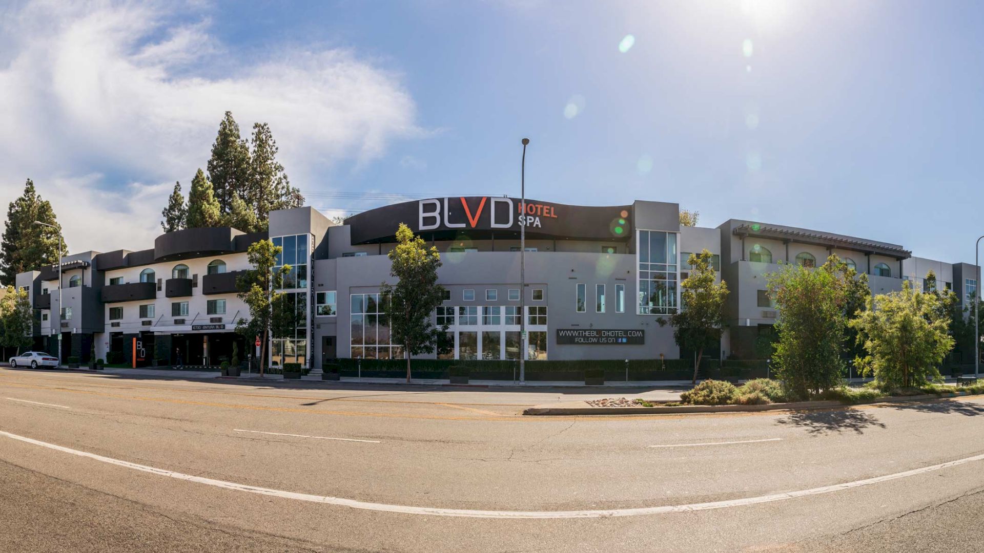 This image shows a modern hotel building with a sign reading "BLVD Hotel & Spa," located along a street with trees and a clear, sunny sky.