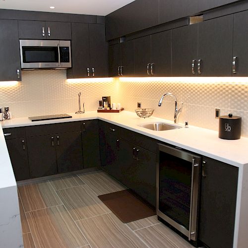 Modern kitchen with dark cabinets, white countertops, stainless steel appliances, under-cabinet lighting, and a tile backsplash ending the sentence.