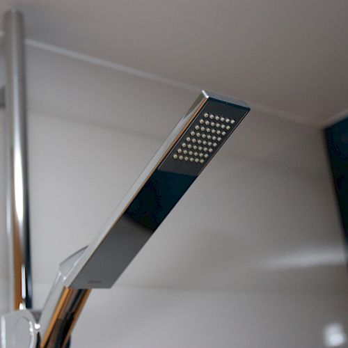 The image shows a modern, rectangular handheld showerhead mounted in a bathroom. The showerhead has a sleek, metallic design.