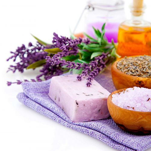 The image shows lavender, a bar of lavender soap, a bowl of dried lavender, and other spa items on a purple cloth, creating a relaxing scene.