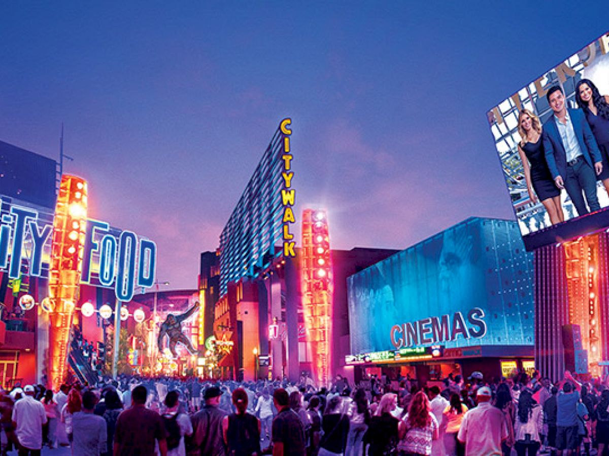 A bustling city area with crowds, bright neon lights, billboards, and signs for CityWalk and cinemas at dusk.