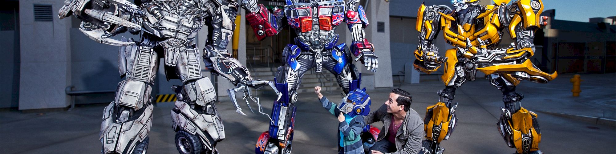 A child and an adult pose with three Transformers characters in front of a 