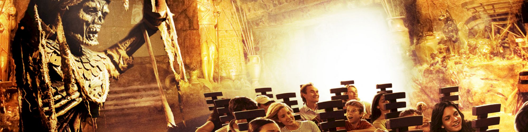 People on an amusement park ride with an Egyptian mummy theme, featuring a skeleton holding a staff over the riders.