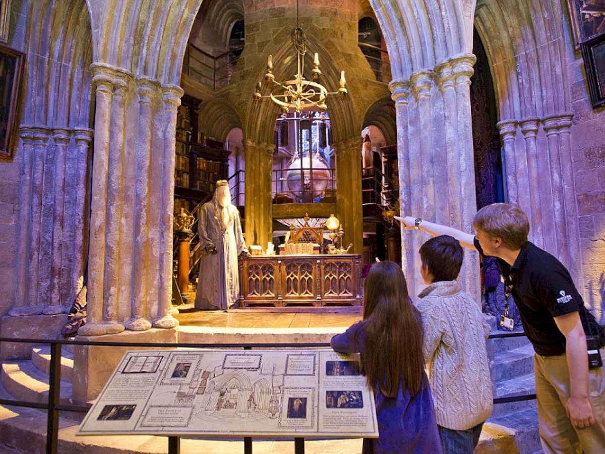 People are looking at a detailed set recreation of a Gothic-style room with tall arches, a statue, and informational displays in front.