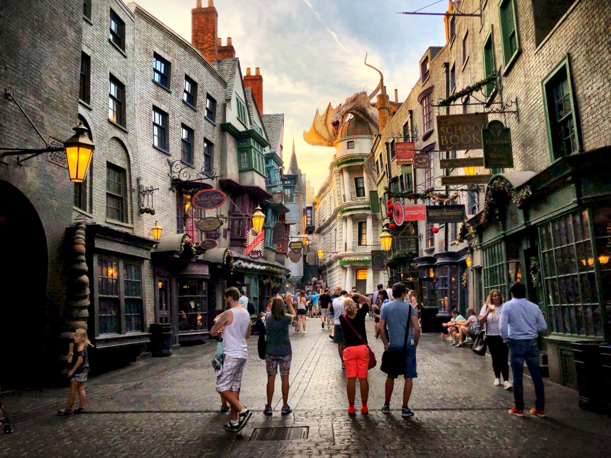 This image shows a bustling street scene with people walking, shops, hanging signs, medieval-style buildings, and a dragon atop one building.