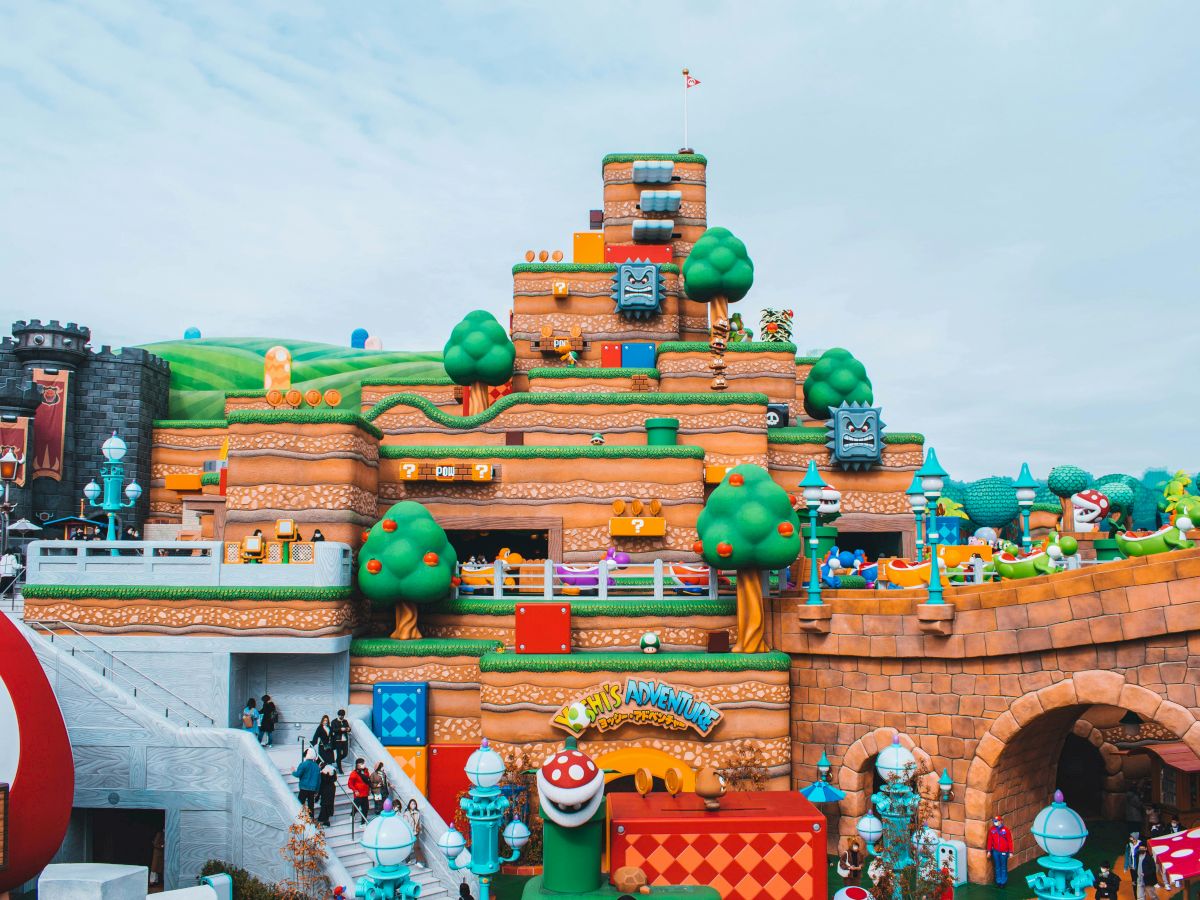 The image depicts a colorful, themed attraction resembling a Mario game world with blocks, characters, and trees, featuring a large hill structure.