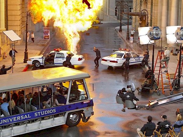 A movie scene with an explosion, police cars, and crew members, captured on a film set at Universal Studios.