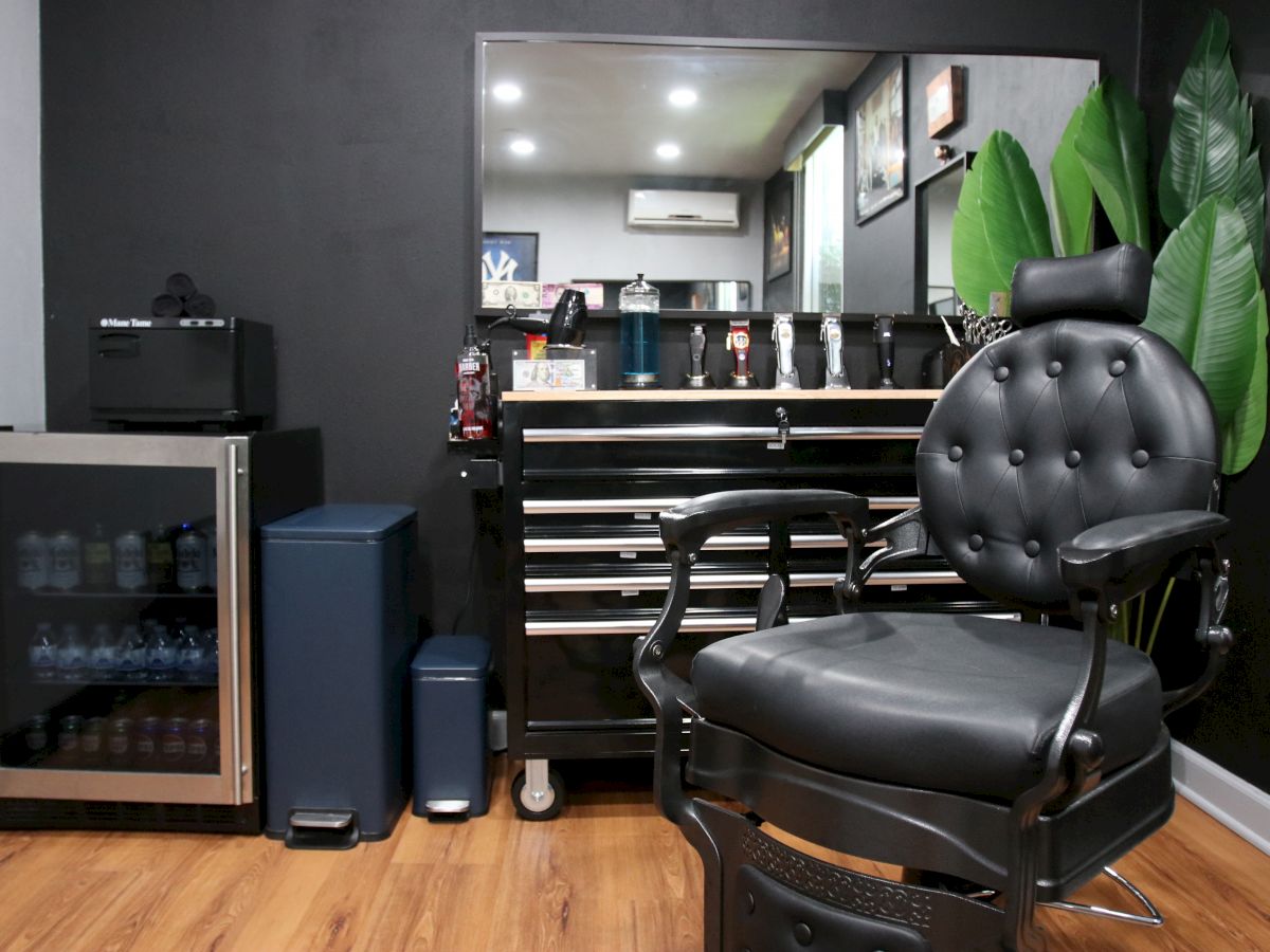 A stylish barber shop interior with a sleek chair, tool cart, fridge, and plants in the corner of the room.