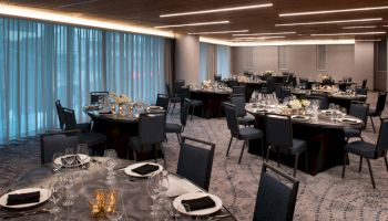 A banquet room setup with round tables, elegant table settings, and dim lighting, ready for a formal event or dining experience.