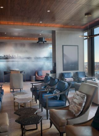 A modern lounge with comfortable seating, large windows with a waterfront view, and a city skyline mural on the back wall.