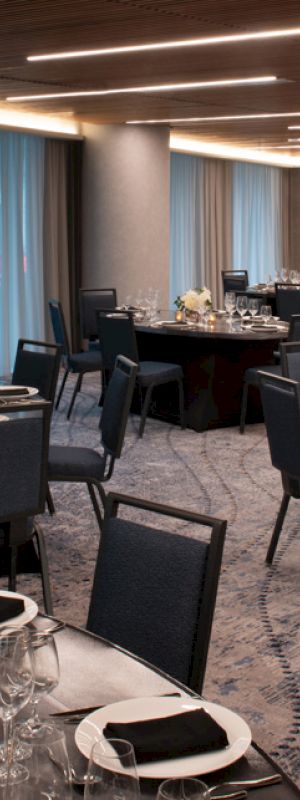 The image shows an elegantly set banquet hall with round tables, arranged with dinnerware, glasses, and flower centerpieces.