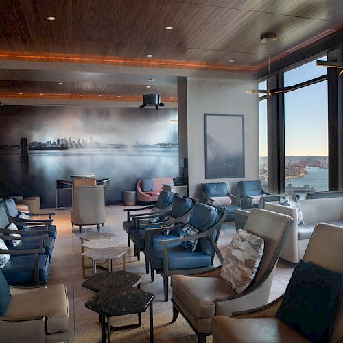 A modern lounge with comfortable seating, panoramic windows offering a city skyline and waterfront view, and contemporary decor.