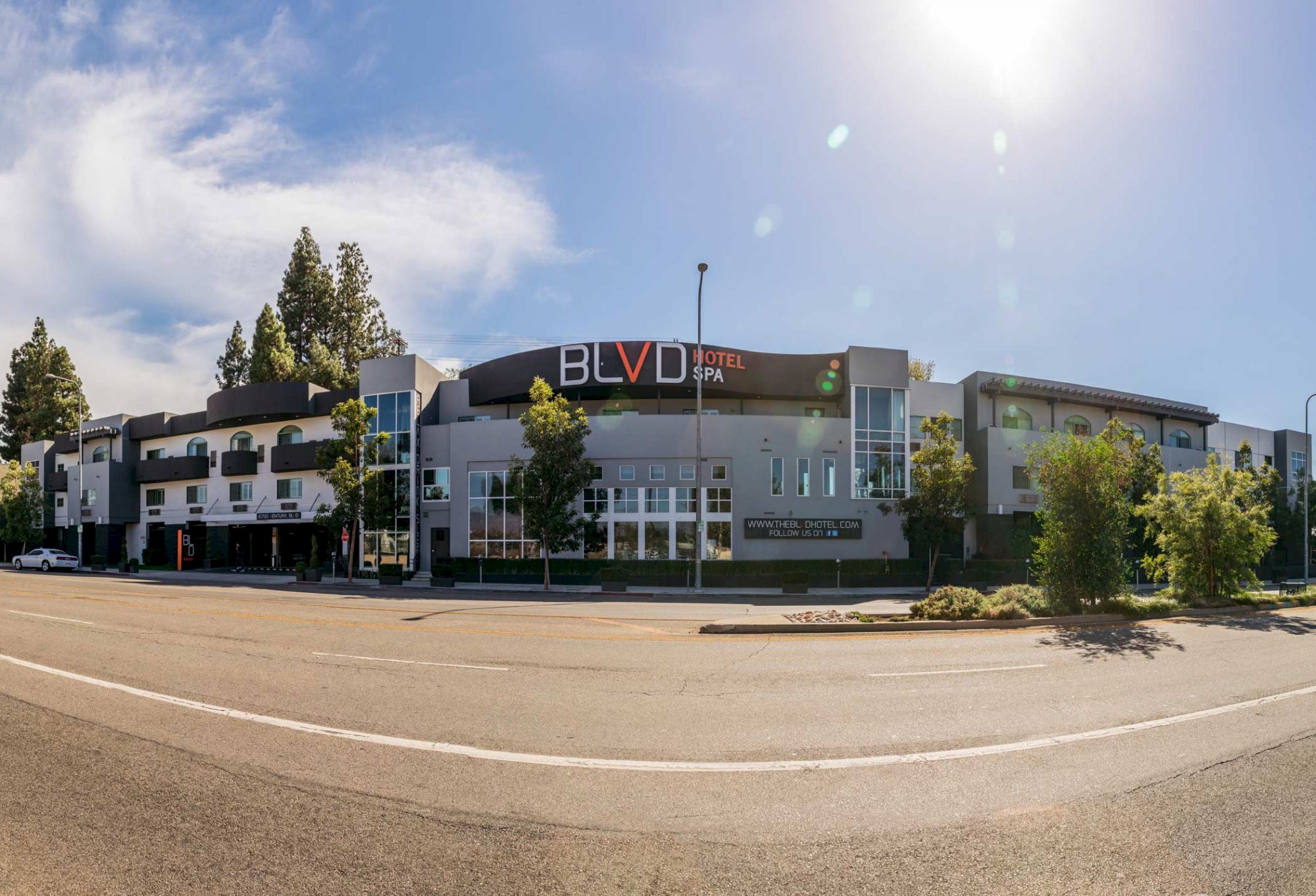 An image of the BLVD Hotel and Spa, showing its exterior with trees and a blue sky in the background.